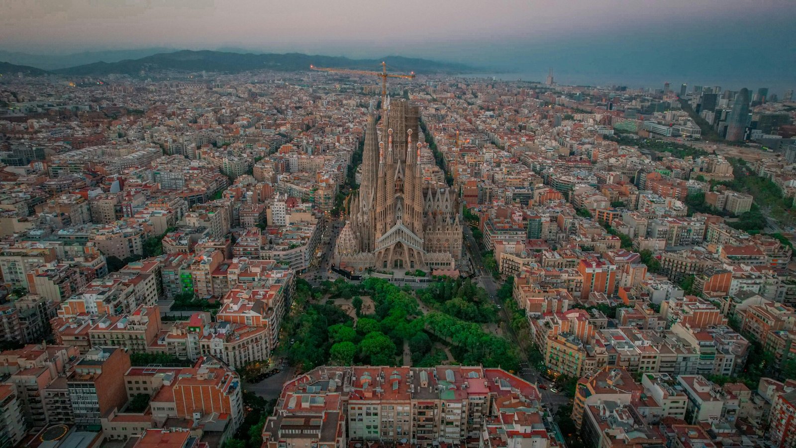 Stunning aerial photo of Sagrada Familia amidst Barcelona cityscape at twilight.